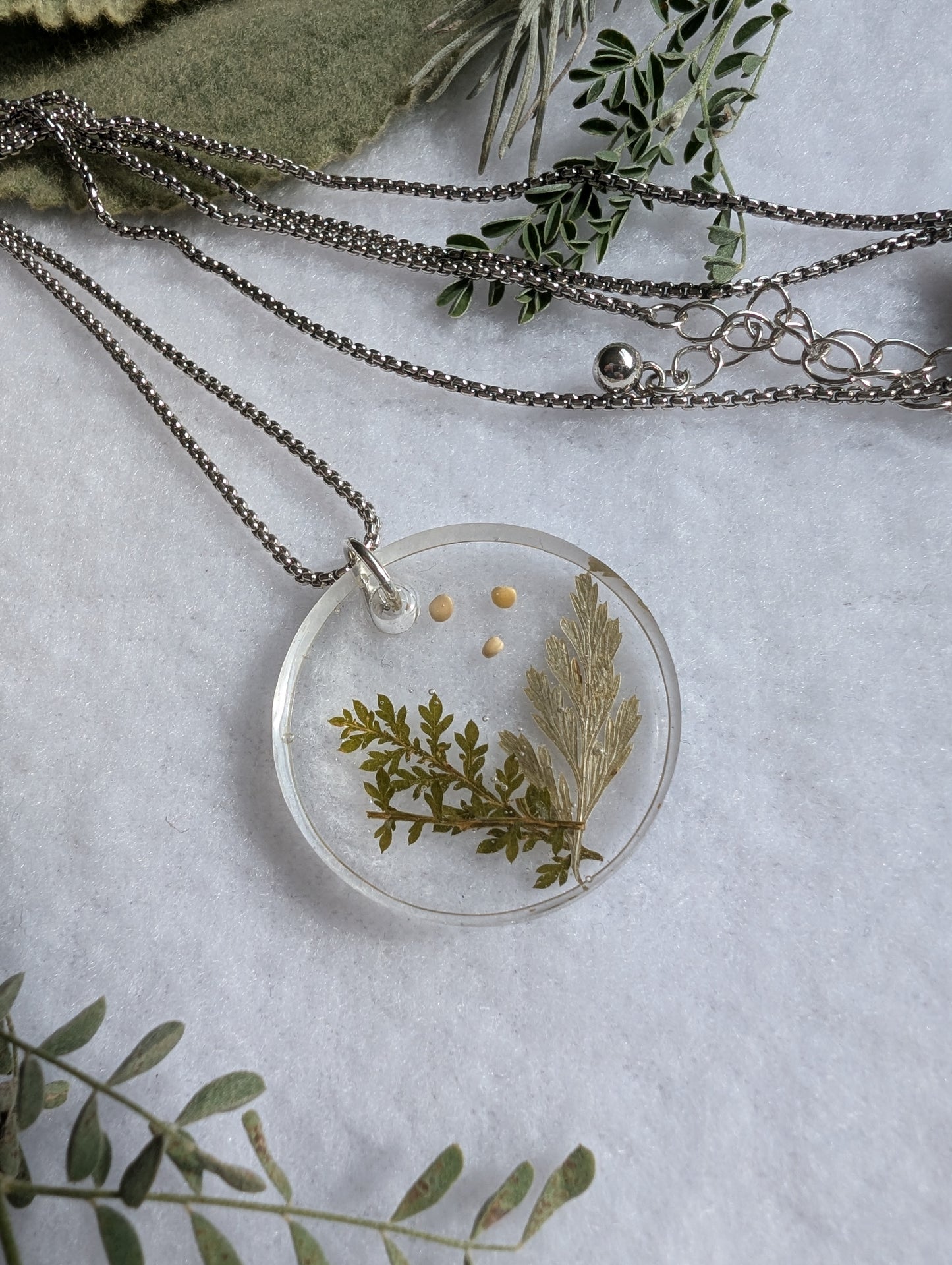 Real pressed leaves alongside 3 mustard seeds cast in a circle pendant with dark silver long chain